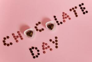 chocola dag belettering gelegd uit van multi gekleurde chocola pillen en pralines Aan roze achtergrond met kopiëren ruimte foto
