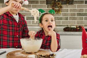 aanbiddelijk jongen kneedt deeg met een houten lepel wanneer zijn schattig jonger zus klimt haar handen in de deeg en smaakt het. charmant Kaukasisch kinderen Koken Kerstmis koekjes samen Bij huis keuken foto