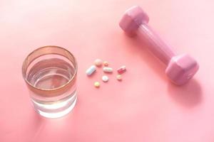 medische pillen, glas water en halter op roze foto