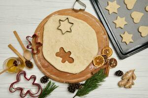 gerold deeg Aan een houten bord met een gesneden figuur van een Mens en gelegd uit peperkoek koekjes Aan een gebakje rek. voorbereidingen treffen voedsel voor de Kerstmis vakantie foto
