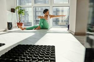 gezond vrouw zittend Aan de verdieping beoefenen en het uitvoeren van yoga poses Bij huis. foto