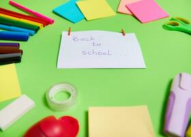 focus Aan een wit papier met belettering terug naar school- in de centrum van multi gekleurde assortiment van schrijfbehoeften kantoor benodigdheden en school- accessoires geregeld in een cirkel. groen achtergrond, kopiëren ruimte foto