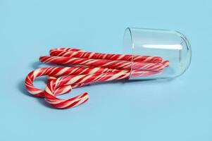 omgekeerd glas aan het liegen Aan een blauw achtergrond met nieuw jaar Kerstmis karamel snoepjes, gestreept snoep wandelstokken, lolly. Kerstmis decoraties voor advertentie Aan web banier foto