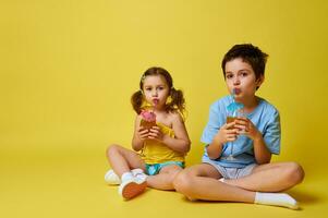 schattig kinderen, jongen en meisje drinken van een rietje een heerlijk cocktail, poseren over- geel achtergrond. kopiëren ruimte foto