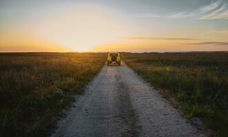 een auto in beweging langs een land steppe weg in de licht van een mooi zonsondergang lucht foto