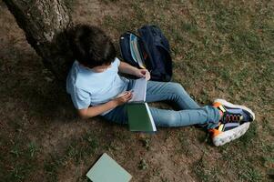 visie van bovenstaande. ijverig spaans slim tiener- school- jongen schrijven, maken aantekeningen Aan schriften, aan het doen huiswerk buitenshuis foto