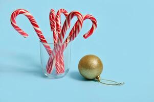 mooi minimalistische gemakkelijk samenstelling met Kerstmis lolly in een transparant glas en gouden Kerstmis bal, Kerstmis boom speelgoed- Aan een blauw achtergrond met kopiëren ruimte voor reclame foto