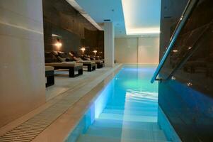 visie van de luxueus modern interieur van de spa en welzijn centrum met zon ligstoelen door de thermisch zwembad met onderwater- verlichting en een waterval. foto