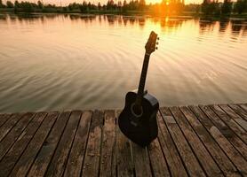 de gitaar staat Aan de kust van de pier, tegen de backdrop van een mooi zonsondergang Aan een warm zomer avond foto