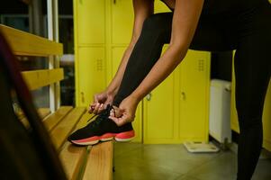 detailopname van een onherkenbaar sportvrouw koppelverkoop schoenveters zetten haar voet Aan een houten bank in Sportschool kastje kamer foto