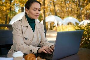 Afrikaanse Amerikaans bedrijf vrouw typen Aan laptop in een Woud cafe terwijl genieten van afgelegen werk in de vers lucht van de platteland weg van de drukte en drukte van de stad. voordelen van ver weg werk foto