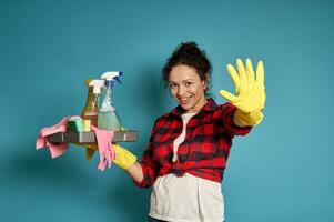 mooi jong vrouw schoonmaak aannemer Holding een emmer met schoonmaak producten en gebaren hou op, staand tegen een blauw achtergrond foto