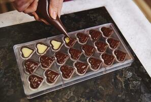 top visie van chocolatier knijpen vulling van romig vloeistof voorbereidingen treffen luxe handgemaakt chocola pralines Bij huis keuken foto