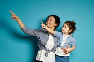 jong glimlachen vrouw en haar schattig weinig dochter richten met wijsvinger Aan blauw achtergrond foto