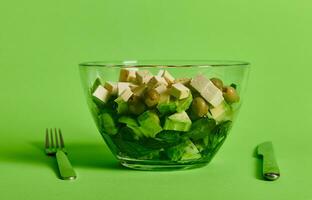 detailopname van een portie kom met groen salade en groenten, en veganistisch tofu kaas Aan groen achtergrond foto