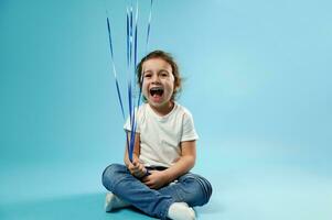 voorkant visie van een schattig meisje lachend en Holding touw van ballonnen zittend Aan blauw achtergrond foto