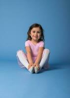 portret Aan een blauw achtergrond van een schattig ballerina in een roze jurk uitrekken haar lichaam foto