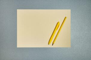 geel kantoor gereedschap Aan een grijs achtergrond. pen, potlood en vel van papier. vlak leggen, kopiëren ruimte, top visie foto