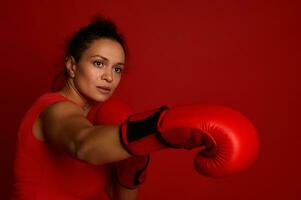 bokser vrouw atleet gevechten in rood boksen handschoenen Aan een rood achtergrond. krijgshaftig kunst concept met kopiëren ruimte voor advertentie voor boksen dag evenement foto