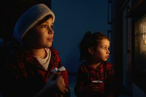 mooi kinderen, jongen in de kerstman hoed en meisje in rood en groen plaid kleren zittend Aan de verdieping en op zoek door de oven Bij de traditioneel Duitse stollen brood gebakken Aan een bakken dienblad foto