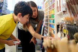 Kaukasisch aanbiddelijk schooljongen vragen de advies van een verkoop manager in kunst winkel, kiezen viltstift pennen van de plank foto