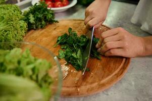 Koken. voedsel en concept van veganisme, kracht en gezond aan het eten - dichtbij omhoog van vrouw hand- snijdend groenten en spinazie bladeren voor salade. gezond ingrediënten voor rauw veganistisch salade foto