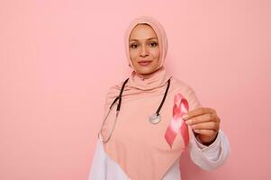 prachtig Arabisch moslim vrouw dokter in roze hijab Holding roze satijn lint, op zoek Bij camera, geïsoleerd Aan gekleurde achtergrond met kopiëren ruimte. wereld dag van strijd borst kanker, 1 st oktober concept foto