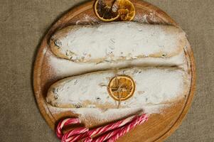 vlak leggen voedsel samenstelling van traditioneel Duitse brood stollen gebakken voor kerstmis, overladen met een droog oranje plak en een touw , snoep wandelstokken Aan een houten bord Aan een linnen tafelkleed foto