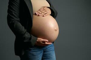 bijgesneden visie. gravid vrouw, verwachtend moeder voorzichtig Holding haar zwanger buik , geïsoleerd over- grijs studio achtergrond. foto