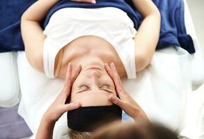 overhead visie van jong vrouw aan het liegen Aan een massage tafel en genieten van professioneel gladmaken en verjongend gelaats massage gedaan door schoonheidsspecialist foto