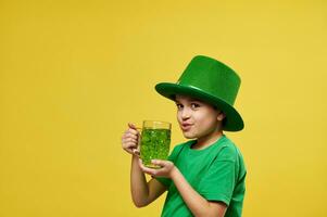 jongen in elf van Ierse folklore hoed drankjes groen drinken terwijl op zoek Bij camera. heilige Patrick dag Aan geel achtergrond met kopiëren ruimte. foto