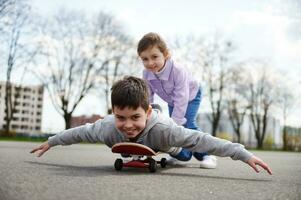 glimlachen meisje rijden haar broer Aan een houten skateboard genieten van een spel samen Aan een sport- grond foto