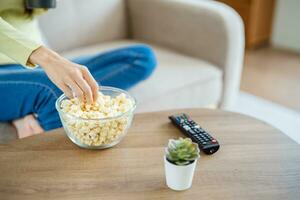 Aziatisch vrouw aan het kijken slim TV en gebruik makend van afgelegen controleur hand- Holding televisie audio afgelegen controle Bij huis met de afgelegen controle televisie foto