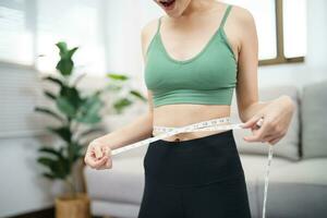 Aziatisch gezond vrouw dieet gewicht verlies. slank vrouw meten taille met meten plakband na eetpatroon Bij huis gewicht controle. foto