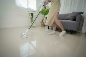 mooi Aziatisch vrouw schoonmaak leven kamer in huis vegen de verdieping gebruik makend van microfiber nat dweilen kussen. huiswerk schoonmaak routine. huiselijk huis houden concept foto