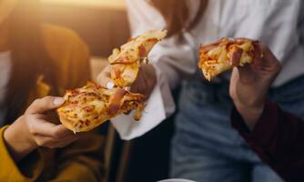 lachend groep van verschillend jong vrouw hangende uit Bij huis samen en aan het eten pizza foto