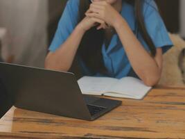 jong Aziatisch vrouw met mooi gezicht, lang haar, blauw overhemd aan het liegen Aan bed in wit slaapkamer Bij huis met kop van koffie en video telefoontje met laptop pratend naar familieleden Aan vakantie. vakantie concept. foto