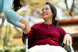 familie verhouding Aziatisch senior vrouw in rolstoel met gelukkig dochter Holding verzorger voor een hand- terwijl uitgeven tijd samen foto