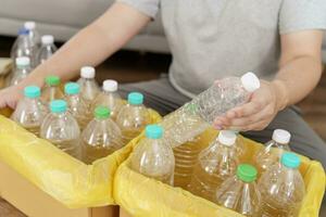 huis recycle eco groen nul concept Mens het werpen leeg plastic fles in recycling bak met geel vuilnis Tassen Bij huis foto