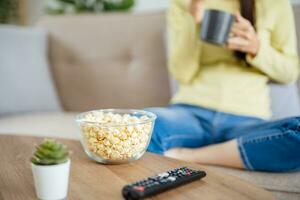 Aziatisch vrouw aan het kijken slim TV en gebruik makend van afgelegen controleur hand- Holding televisie audio afgelegen controle Bij huis met de afgelegen controle televisie foto