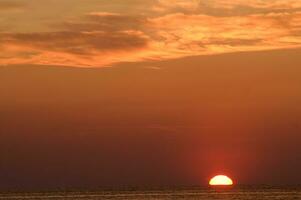 de zon sets over- de oceaan in een bewolkt lucht foto