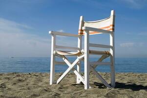 een strand stoel Aan de zand met een blauw lucht foto
