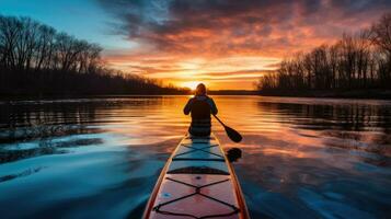 silhouet van mensen Aan peddelen bord Bij zonsondergang Aan kalmte winter rivier- gezien van blauw kajak foto