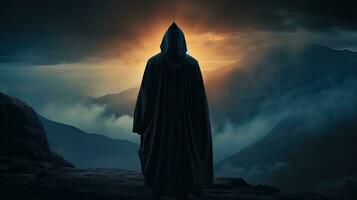 silhouet van een middeleeuws reiziger staand Aan een berg vervelend een met een kap mantel foto