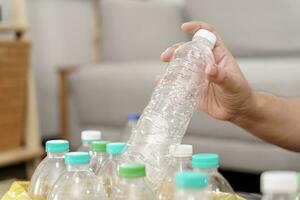 huis recycle eco groen nul concept Mens het werpen leeg plastic fles in recycling bak met geel vuilnis Tassen Bij huis foto