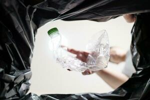 beeld van binnen geel recycling zak van Mens het werpen leeg plastic fles in recycling bak huis recycle eco groen nul concept. foto