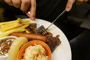 Mens aan het eten gegrild vlees inzet van bord. hand- Holding mes en vork snijdend gegrild rundvlees steak foto