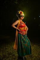 een mooi Sundanees danser poses en dansen in een glamoureus jurk en sjaal in voorkant van de stadium licht foto