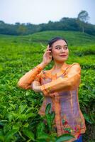 een Javaans vrouw Aan vakantie in een thee tuin vervelend een geel jurk foto