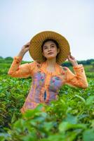 een Javaans vrouw is op zoek na haar thee tuin wanneer ze draagt een oranje jurk foto